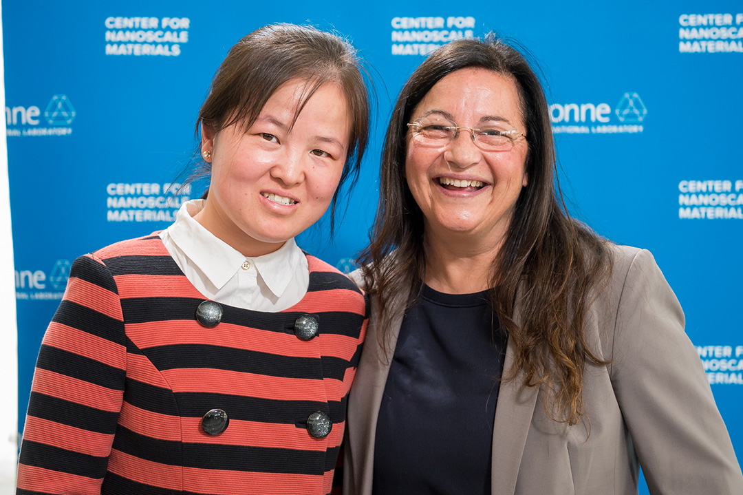 Two smiling women, one with glasses, in front of Blue Argonne logo backdrop.