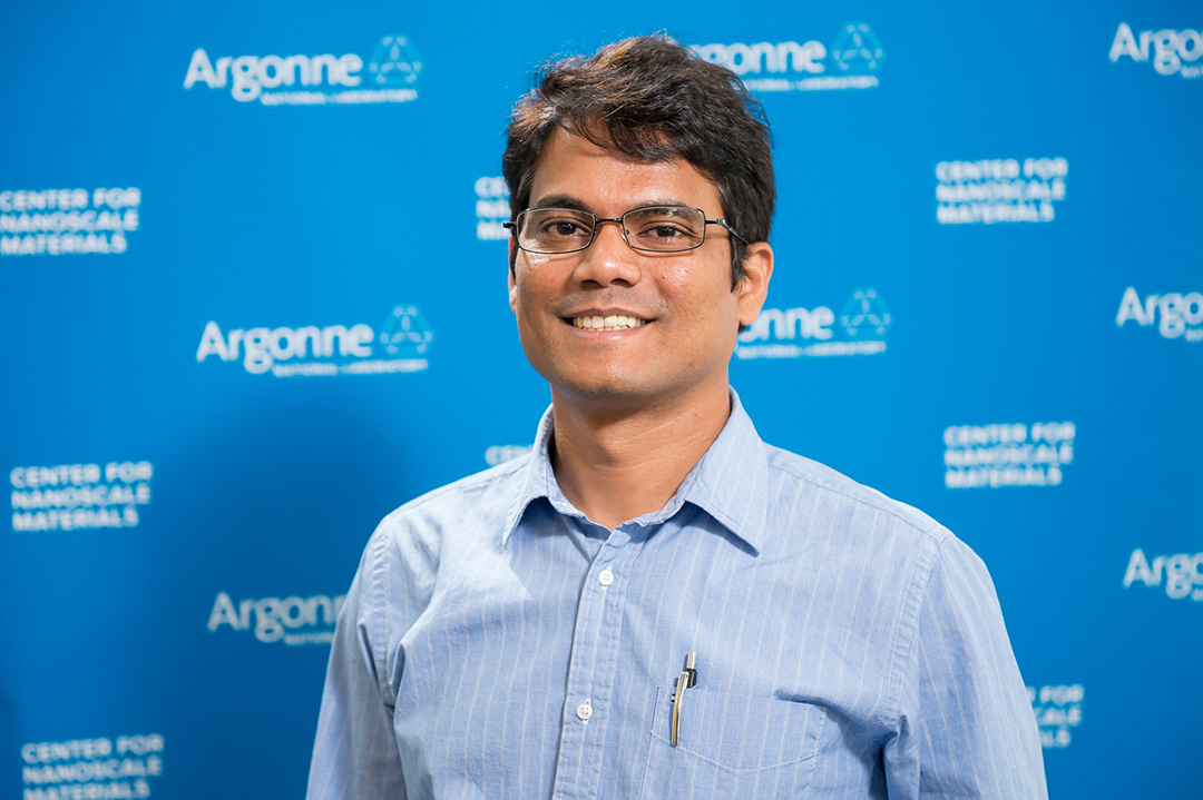 Smiling man wearing glassess, in front of Blue Argonne logo backdrop.