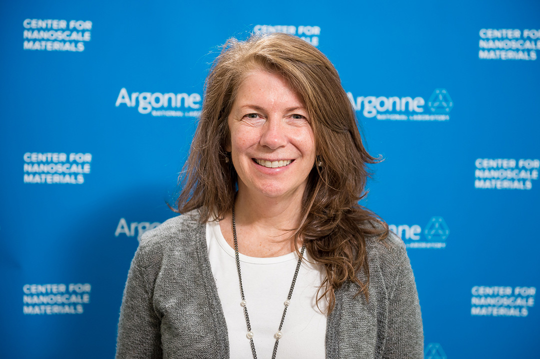 Smiling woman in front of Blue Argonne logo backdrop.