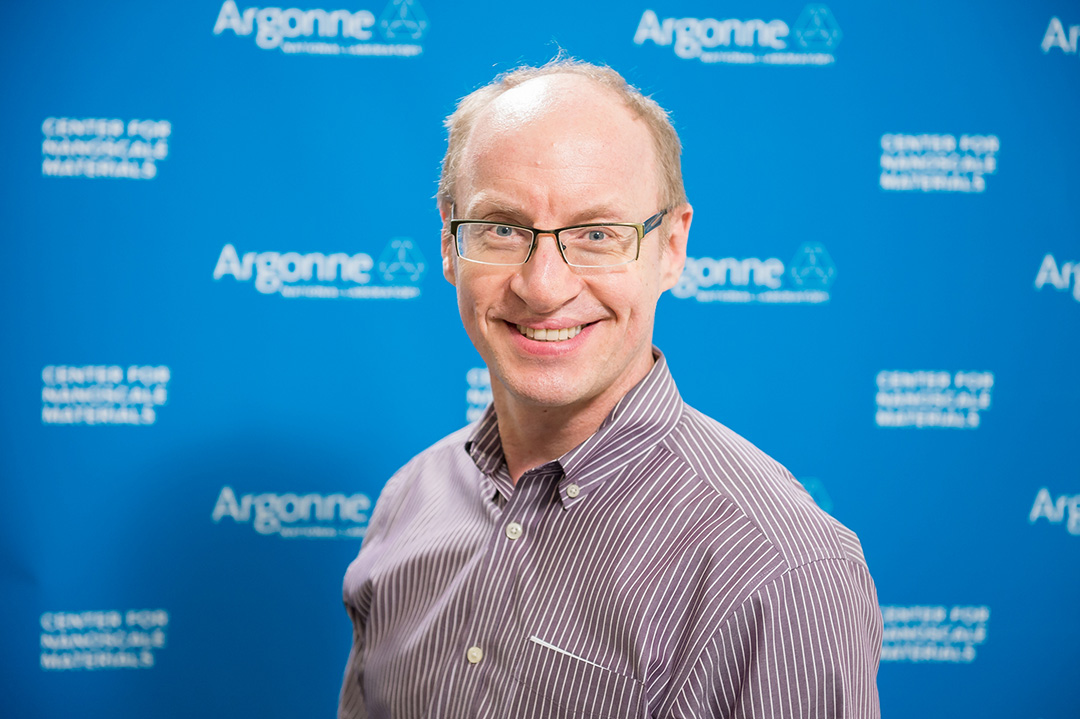 Smiling man wearing glasses, in front of Blue Argonne logo backdrop.
