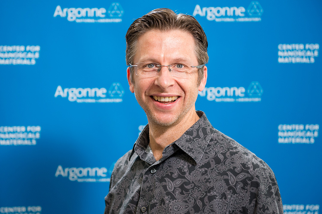 Smiling man wearing glasses in front of Blue Argonne logo backdrop.