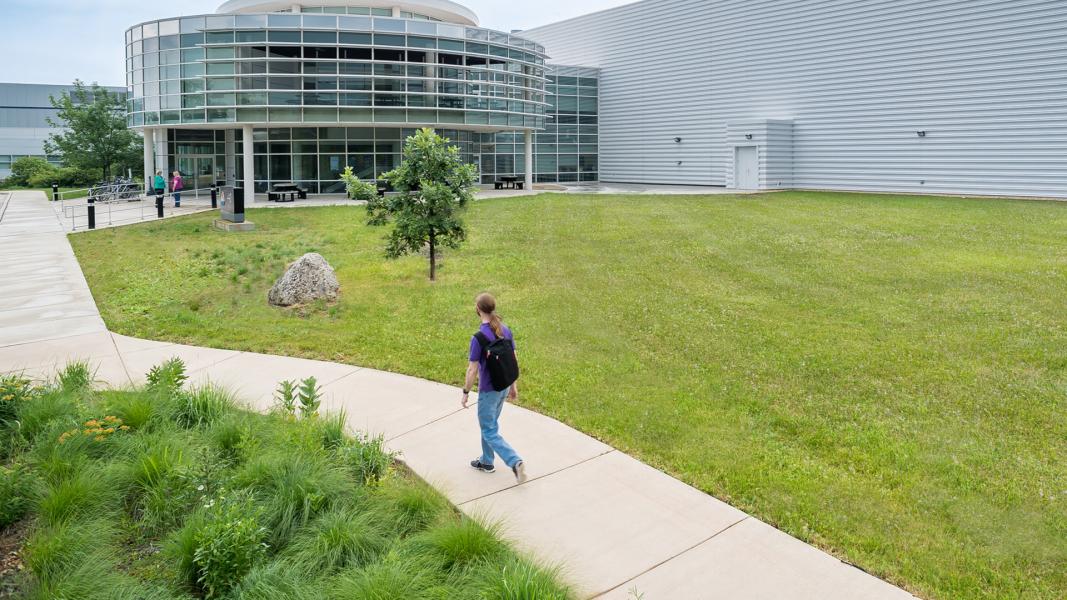 Man walking on sidewalk towards white and glass building.