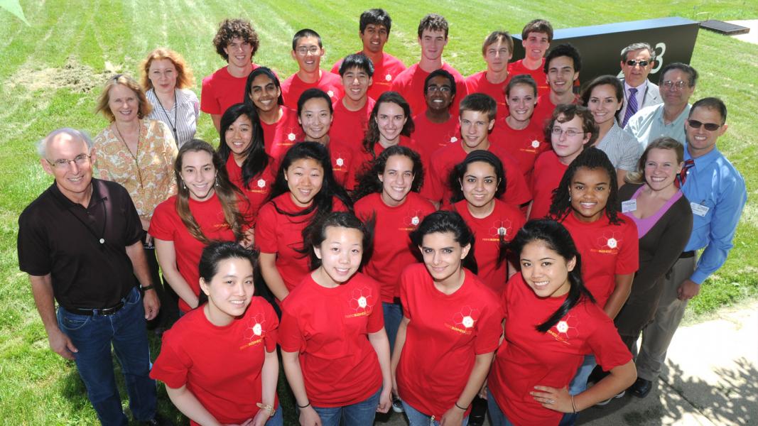 Group of people with students wearing red T-shirts, smiling upwards toward camera.